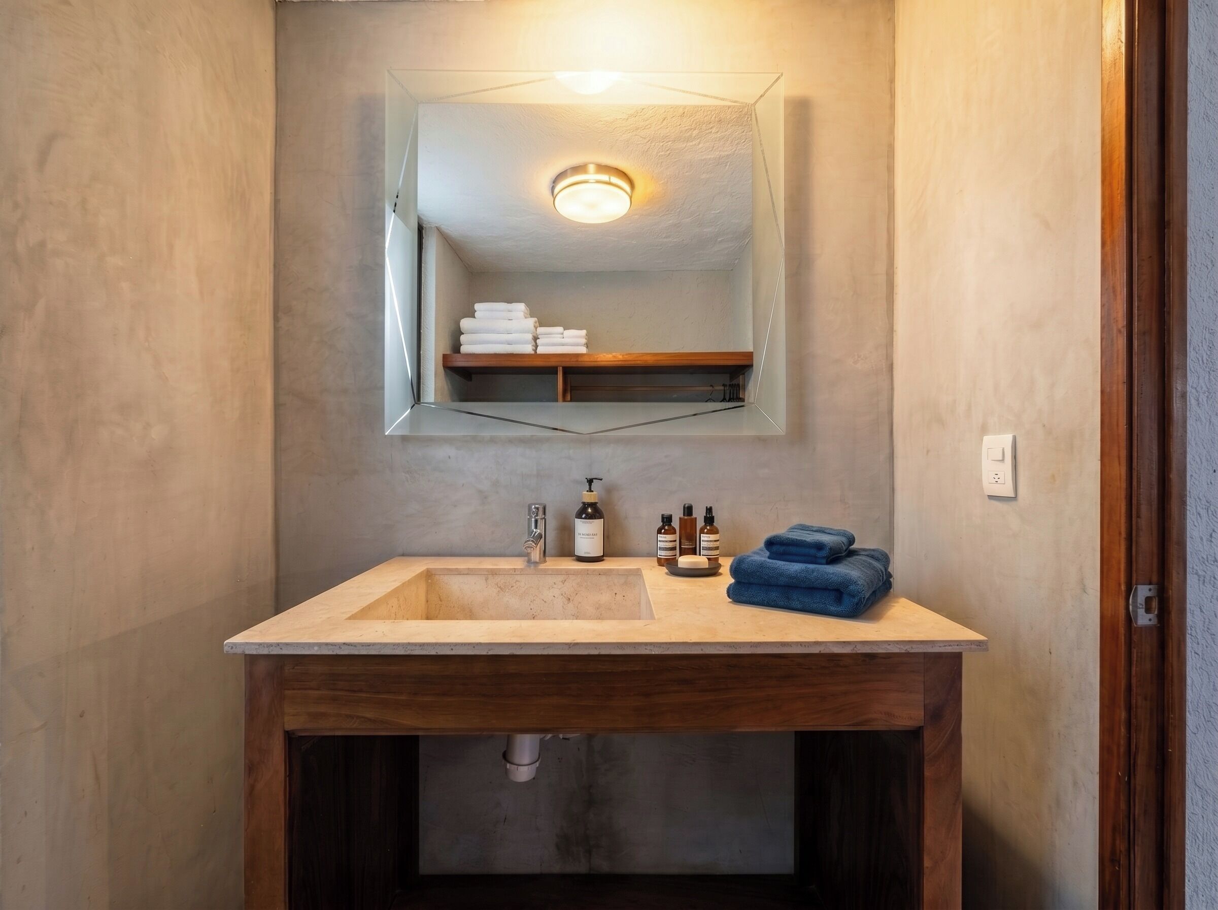 A bathroom with a wooden vanity, a mirror, and a shelf with towels.