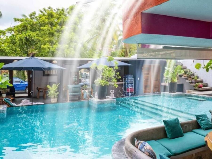 Un área de piscina con cascada, mobiliario de relax y plantas en macetas.
