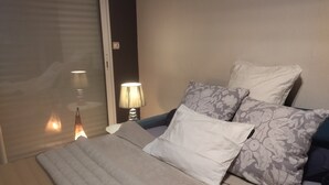 A bedroom with a bed, pillows, a nightstand, a lamp, and a window with blinds.