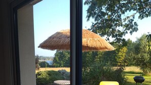 A deck with a thatched umbrella, a yellow chair, and a grill.