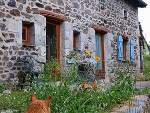 Un bâtiment en pierre doté de nombreuses fenêtres, dont certaines sont pourvues de volets, et une chaise placée à l’extérieur.