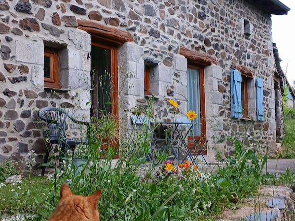 Un edificio de piedra con múltiples ventanas, algunas con contraventanas, y una silla en el exterior.