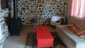 Eine Steinsäule, ein Sofa, ein roter Hocker, eine Lampe und ein Fenster mit Vorhängen.
