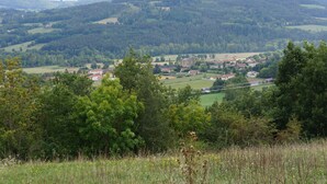 Ländliche Landschaft mit einem Dorf, sanften Hügeln und dichten Wäldern.