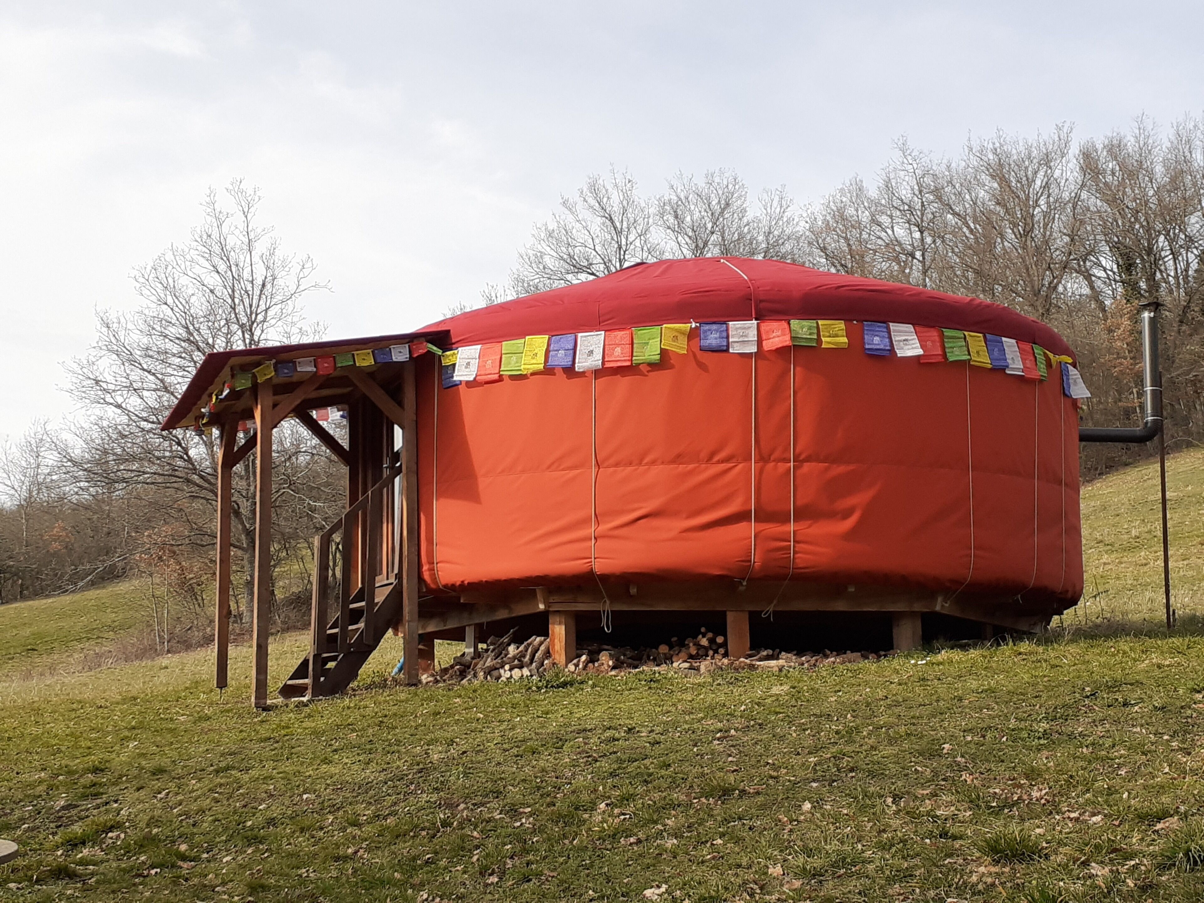 A red yurt with a wooden entrance structure and colorful prayer flags.