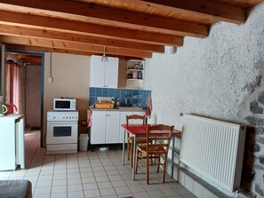 Une cuisine compacte équipée d’un four à micro-ondes, d’une cuisinière et de placards, une table à manger avec des chaises, et un mur en pierre.
