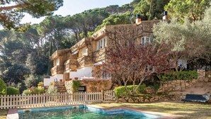 A pool with clear water, a white picket fence, and a building with stone walls and balconies. - Juliola CostaBravaSi - Pool, AC, beach 200 m away (Sant Feliu de Guíxols)