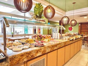 Un espace buffet proposant une variété de plats, une vitrine réfrigérée et des lampes suspendues décoratives.