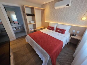 Une chambre d’hôtel équipée d’un lit, d’une armoire, d’une table de chevet et d’un climatiseur fixé au mur.