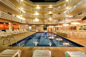 Une piscine intérieure à plusieurs niveaux, dotée de chaises longues et de tables, et entourée de balcons avec des garde-corps.
