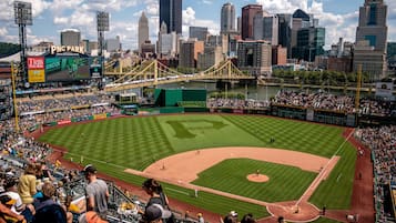 A baseball stadium with a large scoreboard, a city skyline in the background, and a river.