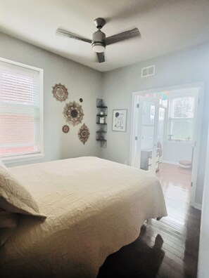 A bedroom with a bed, ceiling fan, decorative wall art, and a door leading to another room.