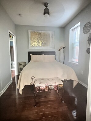 A bedroom with a bed, a bench, a ceiling fan, a window with blinds, and a door leading to another room. - Charming 2-Bd House In Historic Philadelphia Neighborhood (Philadelphia)