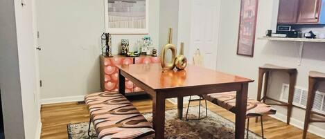 A dining area with a wooden table, benches, a patterned rug, and a chandelier.