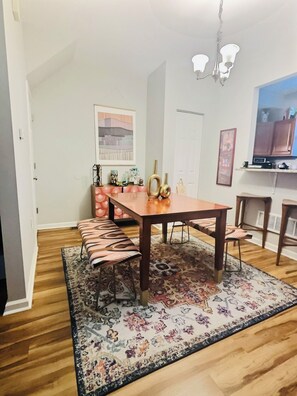 A dining area with a wooden table, benches, a patterned rug, and a chandelier.
