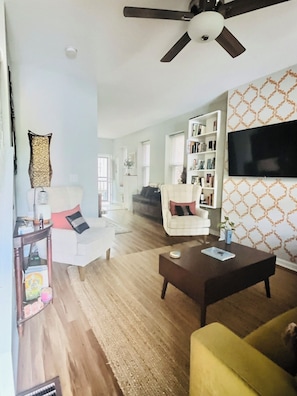 A living room with a ceiling fan, a bookshelf, a television, and a patterned wall.