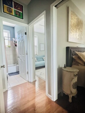 Un couloir au plancher de bois menant à une salle de bain équipée d’une baignoire et d’une douche.