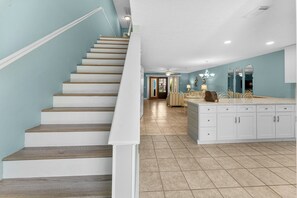 Eine Küche mit einer zentralen Kochinsel, weißen Schränken und einer Treppe mit Holzhinweisen.