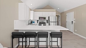 A modern kitchen with white cabinetry, a central island with bar stools, and recessed ceiling lighting. - Modern 1BR Retreat with Garage and Yard (Coeur d'Alene)