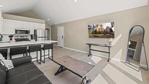 A modern kitchen with white cabinets, a central island, and a dining area with a sofa and coffee table. - Modern 1BR Retreat with Garage and Yard (Coeur d'Alene)
