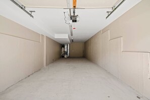 Een gang met beige wanden en een betonnen vloer, die leidt naar een deur aan het einde.