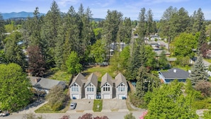 A residential area with a row of three-story houses, surrounded by dense trees and a clear sky. - Modern 1BR Retreat with Garage and Yard (Coeur d'Alene)