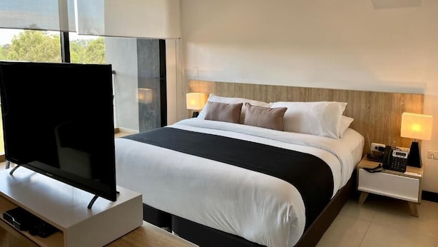 Una habitación de hotel moderna con una cama grande, un televisor de pantalla plana, lámparas de noche y un ventanal con vistas.