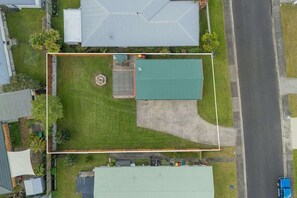 An aerial view of a residential area with houses, a green lawn, and a paved driveway. - Hosts on the Coast Our Little Gem (Whitianga)