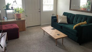 Een woonkamer met een groene bank, een houten salontafel, een rode poef, een klein bijzettafeltje en een potplant.
