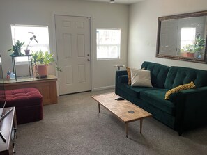 A living room with a green sofa, a wooden coffee table, a red ottoman, a small side table, and a potted plant. - Cozy First Floor Studio in Neighboorhood Dublex (Atlanta)