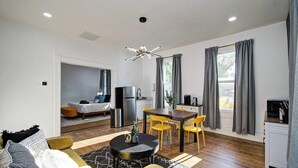 Un salon moderne comprenant un canapé, une table basse et un coin repas avec des chaises. Il y a aussi une cuisine équipée d’un réfrigérateur et d’un four à micro-ondes.