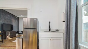 Une cuisine moderne avec un réfrigérateur en acier inoxydable, des meubles blancs et une fenêtre avec des rideaux.