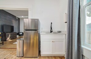 Eine moderne Küche mit einem Edelstahlkühlschrank, weißen Schränken und einem Fenster mit Vorhängen.