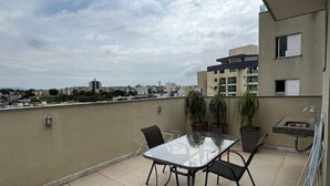 A rooftop terrace with a glass table and chairs, potted plants, and a small sink.