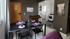 A dining area with a table set for four, a piano, and a kitchen in the background.