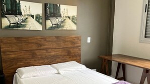 A bedroom with a bed, a wooden headboard, a bench, and two wall-mounted pictures.
