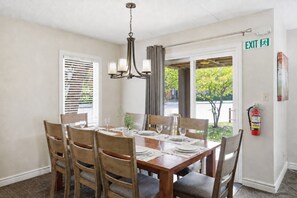 A dining area with a wooden table set for four, a chandelier, and a fire extinguisher on the wall. - Village Side 3BDR | New Kitchen & Private Patio (The Blue Mountains)