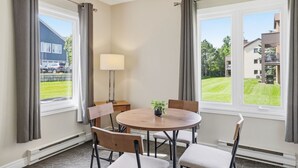 Ett hotellrum med ett runt bord, fyra stolar, en lampa och utsikt över en grön gräsmatta och byggnader.