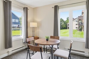 Ein Hotelzimmer mit einem runden Tisch, vier Stühlen, einer Lampe und Blick auf eine grüne Wiese und Gebäude.