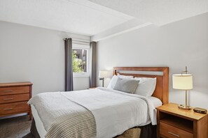 Ein Hotelzimmer mit Bett, Nachttisch, Lampe und Blick ins Freie.