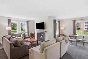 A hotel room with a fireplace, a television, a sofa, a dining table, and a view of the outdoors. - Village Side 3BDR | New Kitchen & Private Patio (The Blue Mountains)