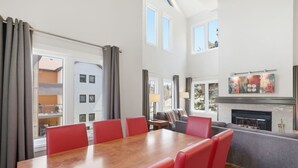 Una habitación de hotel con una mesa de comedor, sillas rojas, un sofá, una chimenea y ventanas grandes.
