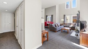 Un espacio habitable amplio con un sofá, una mesita de centro y un televisor. Hay una zona de comedor con sillas rojas y una mesa.
