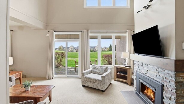 A spacious living room with a fireplace, a television mounted on the wall, and a large sliding glass door leading to a backyard. - Ground-Floor Home with Sauna on Monterra Golf (The Blue Mountains)