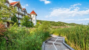 A wooden boardwalk leading to a building with a red roof, surrounded by lush greenery and hills in the background. - Ground-Floor Home with Sauna on Monterra Golf (The Blue Mountains)