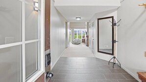 A hallway with a door, a coat rack, and a view into a room with a chair and a table. - Ground-Floor Home with Sauna on Monterra Golf (The Blue Mountains)