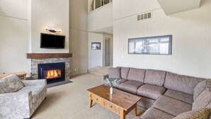 Ein geräumiges Wohnzimmer mit Kamin, einer großen Couch, einem Couchtisch und einem flachbildfernseher, der über dem Kamin angebracht ist.