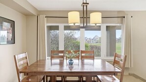 Ein Esszimmer mit einem Holztisch, vier Stühlen, einer Blumenvase und Blick auf Häuser durch große Fenster.