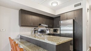 Una cocina moderna con armarios de madera oscura, electrodomésticos de acero inoxidable, encimeras de granito y una isla integrada con asientos tipo barra.