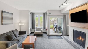 Habitación de hotel con sofá, sillón, televisor de pantalla plana, chimenea y puerta corredera que da a un patio.